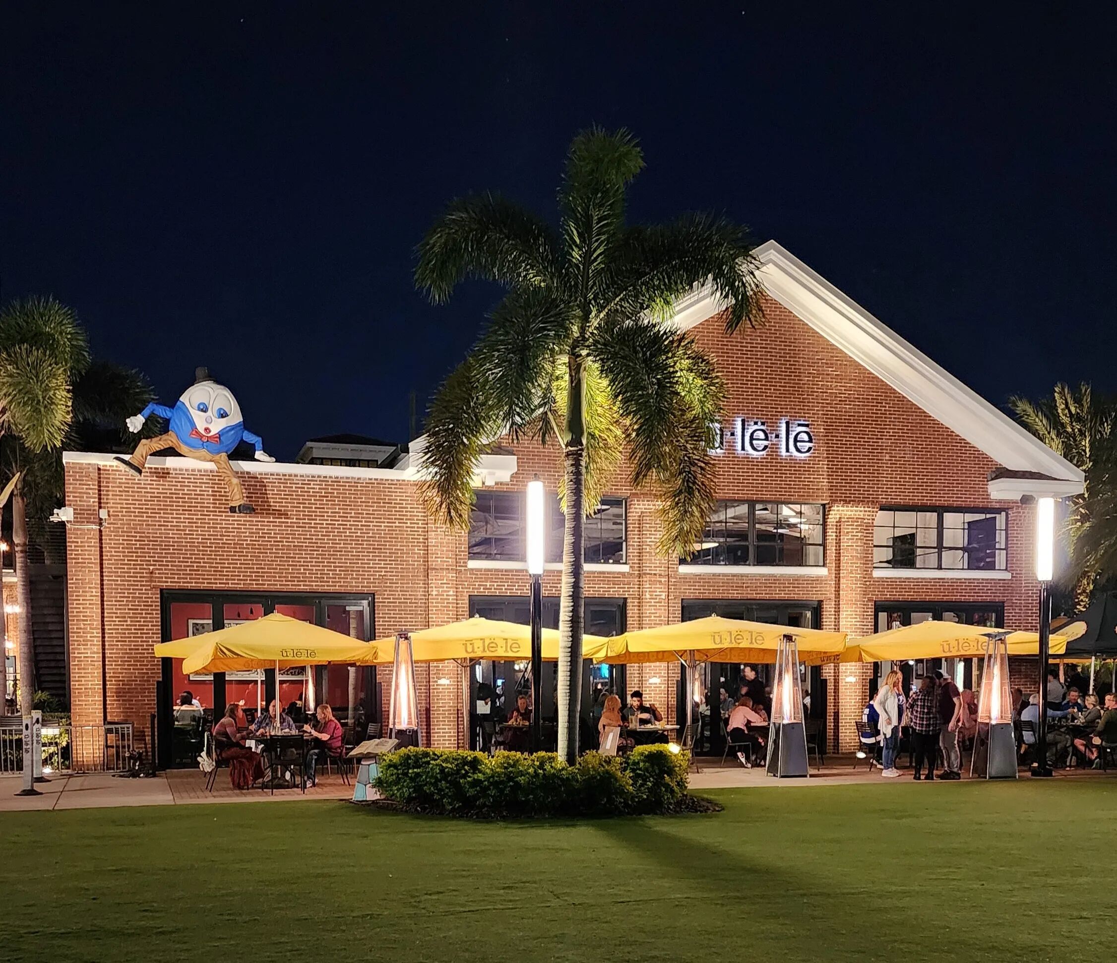 A brick building with outdoor seating and yellow umbrellas, featuring a large mascot on the roof.