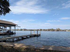 A dock extending into calm water with a covered seating area and a clear view of a residential area in the background. - Beautiful views at LBJ Lakehouse with double lot (Granite Shoals)