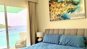 Un dormitorio con una cama grande, un ventilador de techo, un cuadro y vistas al mar.