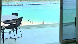 Balcón con vista a una playa y un muelle, con una mesa y sillas.