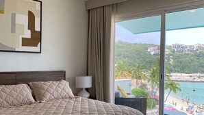 A hotel room with a large bed, a ceiling fan, a view of a beach, and a painting on the wall. - Stunning Beachfront Property (Crucecita)
