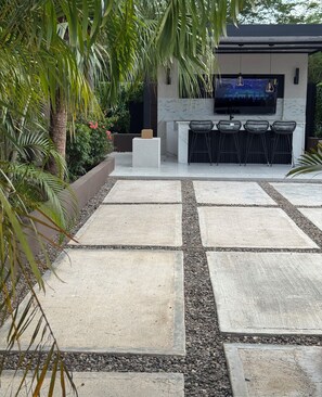 An outdoor patio area with a stone floor, a seating arrangement, and a flat-screen TV mounted on the wall. - Luxury Oasis of New Harbour Village III (St. Catherine Parish)