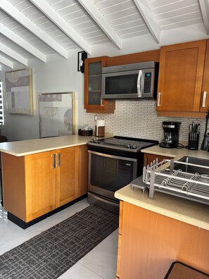 A modern kitchen with wooden cabinets, a stainless steel stove, a microwave, and a coffee maker. - Luxury Oasis of New Harbour Village III (St. Catherine Parish)