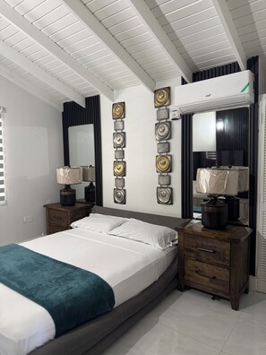 Un dormitorio con cama, mesitas de noche, aire acondicionado de pared y decoración en la pared.
