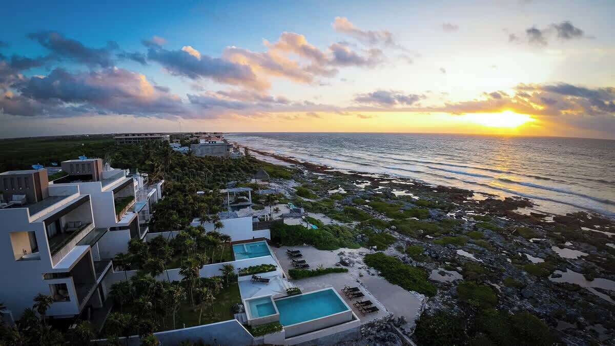A coastal hotel with modern architecture, a swimming pool, and a view of the ocean at sunset.