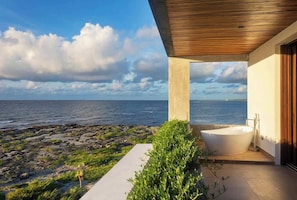 A modern outdoor bathroom with a large bathtub, a concrete structure, and a view of the sea. - Valina (Tulsayab)