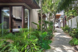 A pathway leading to a modern building with glass doors, surrounded by lush tropical plants. - Valina (Tulsayab)