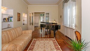 A living room with a piano, a sofa, a rug, and a plant. - Villa Cecilia, facing Lucca's ancient city walls! (Lucca)