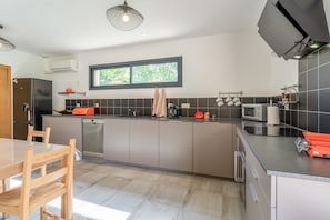 Una cocina moderna con comedor, que cuenta con una isla grande, electrodomésticos integrados y un ventanal que proporciona luz natural.