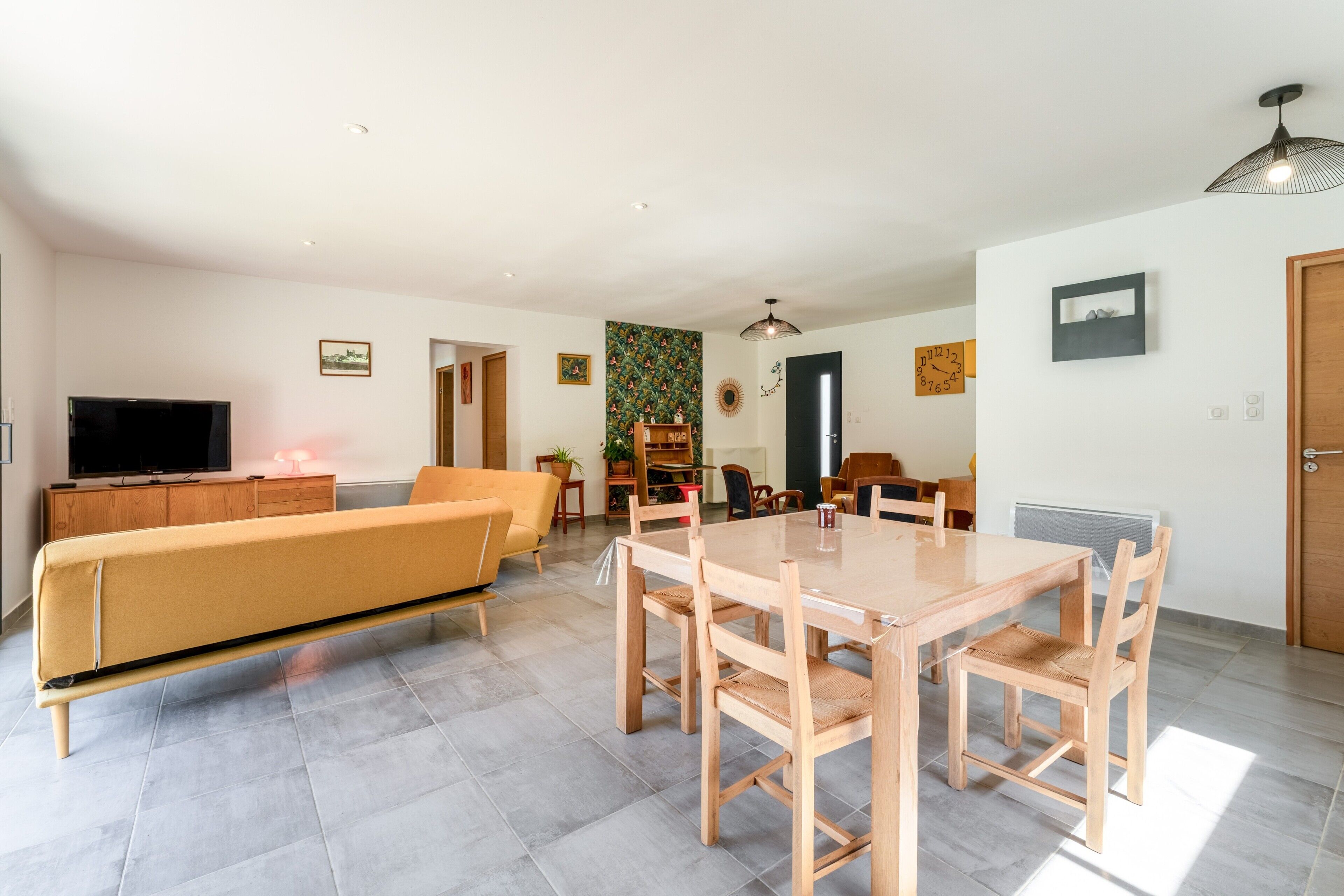 Una sala moderna con sofá, mesa de comedor, sillas, televisor y una zona de cocina.