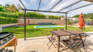 A covered outdoor area with a pool, a barbecue grill, and a dining table with chairs.