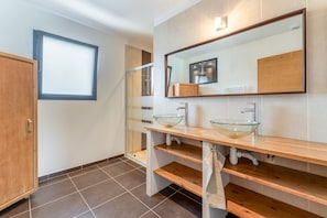Un baño moderno con un lavabo de vidrio, tocador de madera, un espejo grande y una ventana.