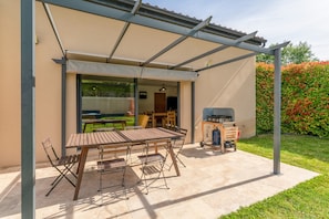 Un patio exterior con mesa y sillas, una parrilla y una zona cubierta.