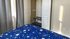 Un dormitorio con cama, armario con ropa colgada y ventana con cortinas.