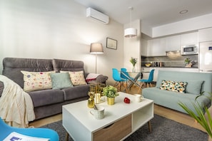 A modern living room with a grey sofa, blue chairs, a white coffee table, and a kitchen area with a microwave and refrigerator. - Central Apartment in Seville with Wi-Fi, Air Conditioning, and Optional Parking (Sevilla)