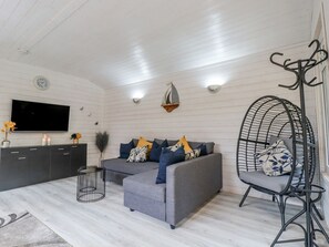 Sala moderna com sofá cinza, cadeira de metal preto, televisão e parede decorativa com relógio e pequeno enfeite de navio.