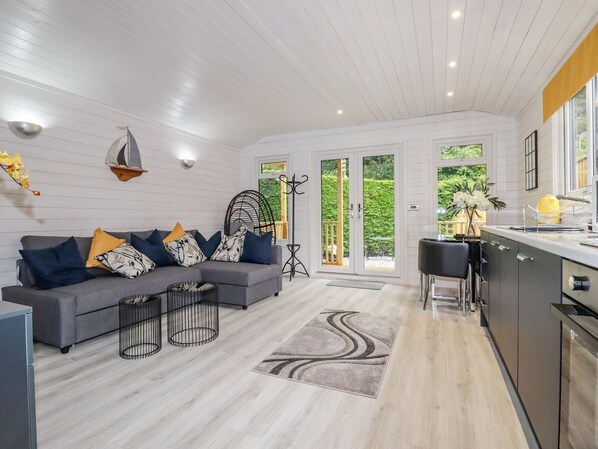 Uma sala de estar moderna com um sofá cinza, almofadas estampadas em preto e branco, uma mesinha lateral de metal preto e um tapete cinza.