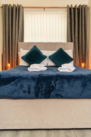 Ein ordentlich gemachtes Bett mit einem dunkelblauen Überwurf, zwei Kissen und gefalteten Handtüchern.
