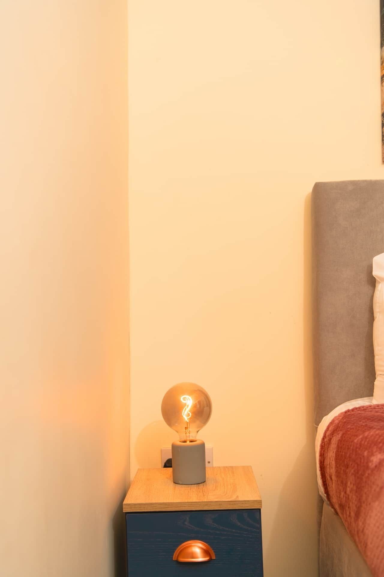 A bedside table with a lamp, a drawer, and a bed with a headboard.