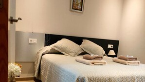 Una cama bien hecha con almohadas y toallas dobladas, una lámpara de noche y un cuadro en la pared.
