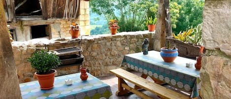 Un espacio de comedor al aire libre rústico con paredes de piedra, bancos de madera y plantas en macetas.