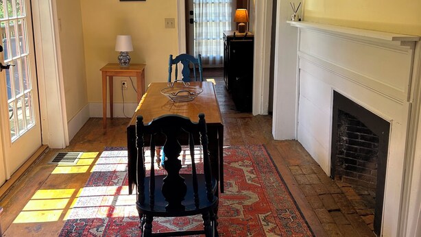 A dining room with a wooden table, chairs, a patterned rug, a fireplace, and a door leading to another room. - Historic Cape in quaint village of Jefferson Maine (Jefferson)