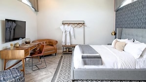 A modern hotel room with a bed, a desk, a chair, a TV, and a coat rack with clothes. - New 3BR Apartment in Riga, Latvia (Riga)