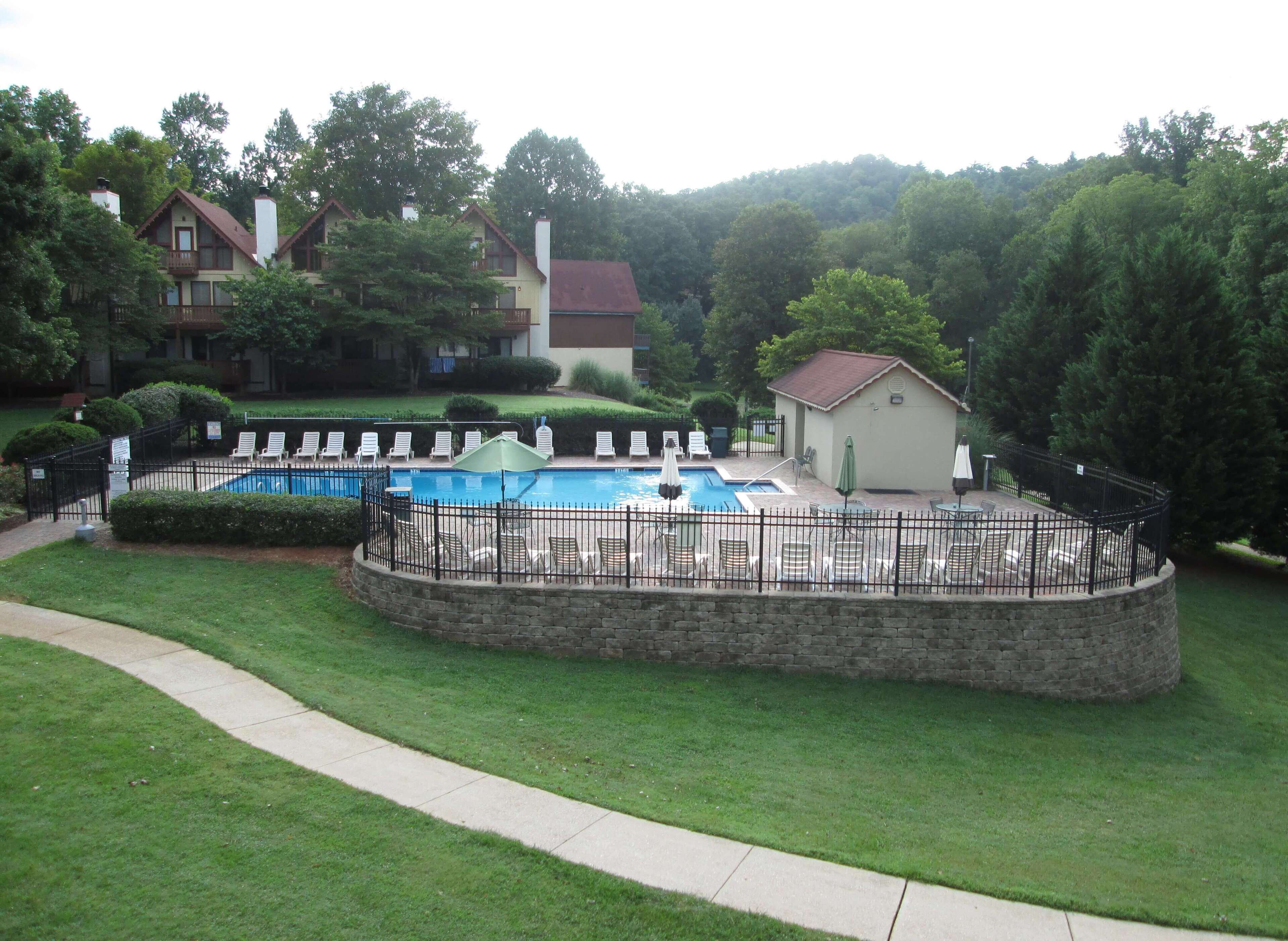 A swimming pool with lounge chairs and a small building, surrounded by a stone wall and greenery.