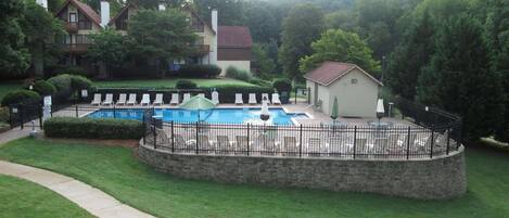 A swimming pool with lounge chairs and a small building, surrounded by a stone wall and greenery.