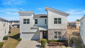 Een modern woonhuis met twee verdiepingen, een stenen gevel, een garage en een verzorgd gazon.