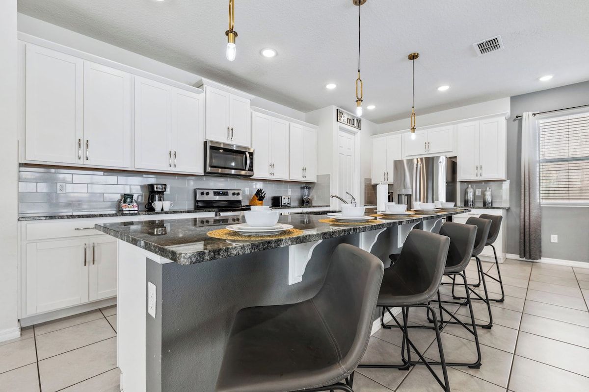 A modern kitchen with white cabinets, stainless steel appliances, and a central island with bar stools.