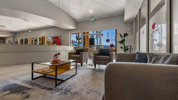Eine großzügige Lobby mit modernem Design, inklusive einer Sitzecke mit Sofas und einem Couchtisch, einem Empfangsbereich und großen Fenstern mit Blick ins Freie.