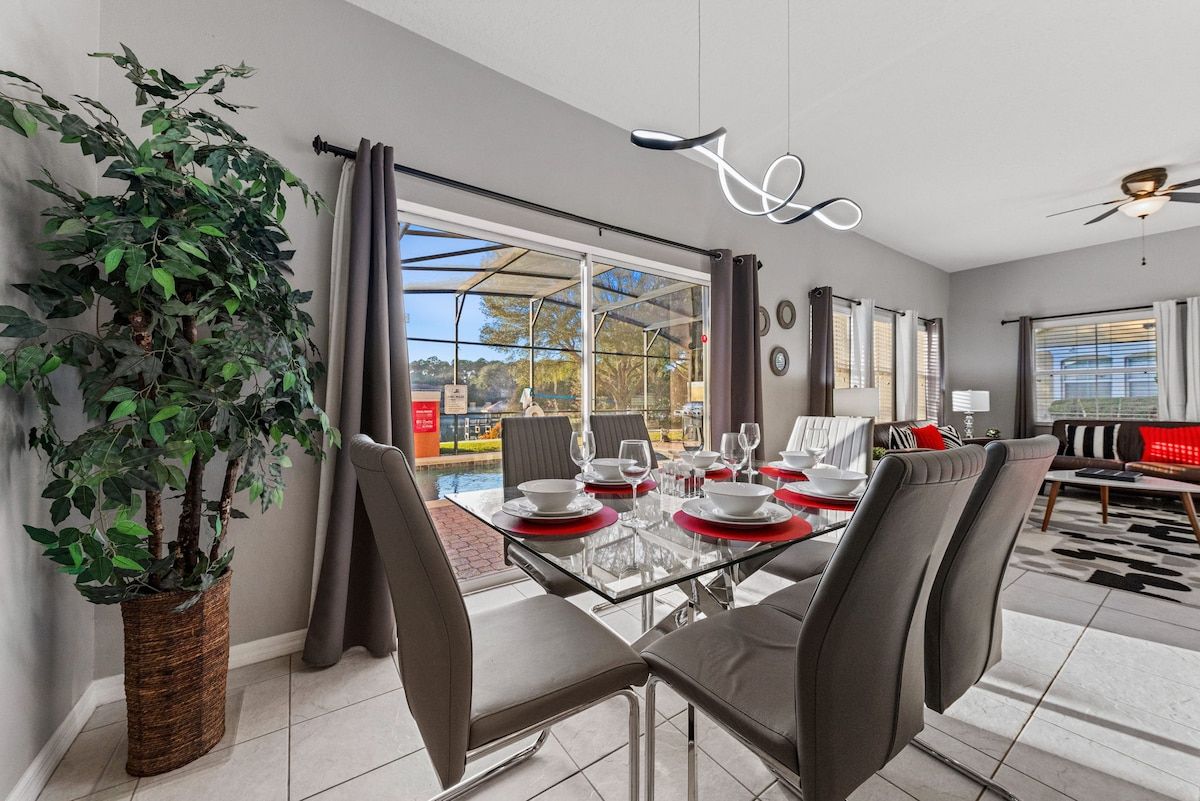 A modern dining area with a glass table, grey chairs, and red placemats.