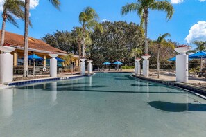 A swimming pool with a tiled edge, surrounded by palm trees and blue umbrellas. - Themed rooms • Pvt pool • BBQ • Near Disney (Kissimmee)