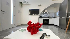 Une cuisine moderne avec un plan de travail blanc, un objet décoratif rouge, une télécommande et un téléviseur fixé au mur.