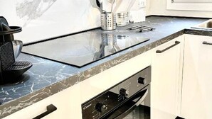 Une cuisine dotée d’un plan de travail noir, de meubles blancs, d’un four encastré et d’une hotte en acier inoxydable.