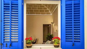 Une porte d’entrée avec des volets bleus, qui donne sur un espace intérieur doté d’un plafond en briques et où l’on aperçoit une autre porte.