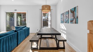 Un salon moderne avec un canapé de couleur turquoise, un plancher en bois, une table centrale avec des bancs, un luminaire suspendu et des œuvres d'art abstraites accrochées au mur.