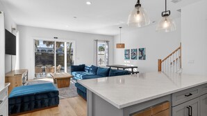 Une cuisine moderne dotée d’un grand îlot central, d’un coin repas avec un canapé bleu et d’une vue sur l’extérieur.