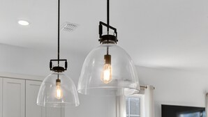 Une cuisine moderne avec des armoires blanches, un banc en bois et des luminaires suspendus dotés d’ampoules apparentes.