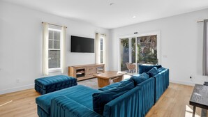 Un salon moderne avec un grand canapé d’angle, une table basse en bois et un téléviseur fixé au mur.