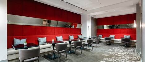 A modern hotel lobby with red upholstered seating, a carpeted floor, and a central area with tables and chairs.