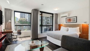 Una habitación de hotel moderna con una cama grande, una mesa de centro de vidrio, un escritorio y una silla.