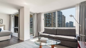 A modern living room with a glass coffee table, grey sofa, and a view of high-rise buildings. - Modern Studio Suite in Yaletown w/ Access to Pool (Vancouver)
