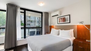 Habitación de hotel moderna con una cama grande, una mesita de noche, una lámpara y vistas al exterior.