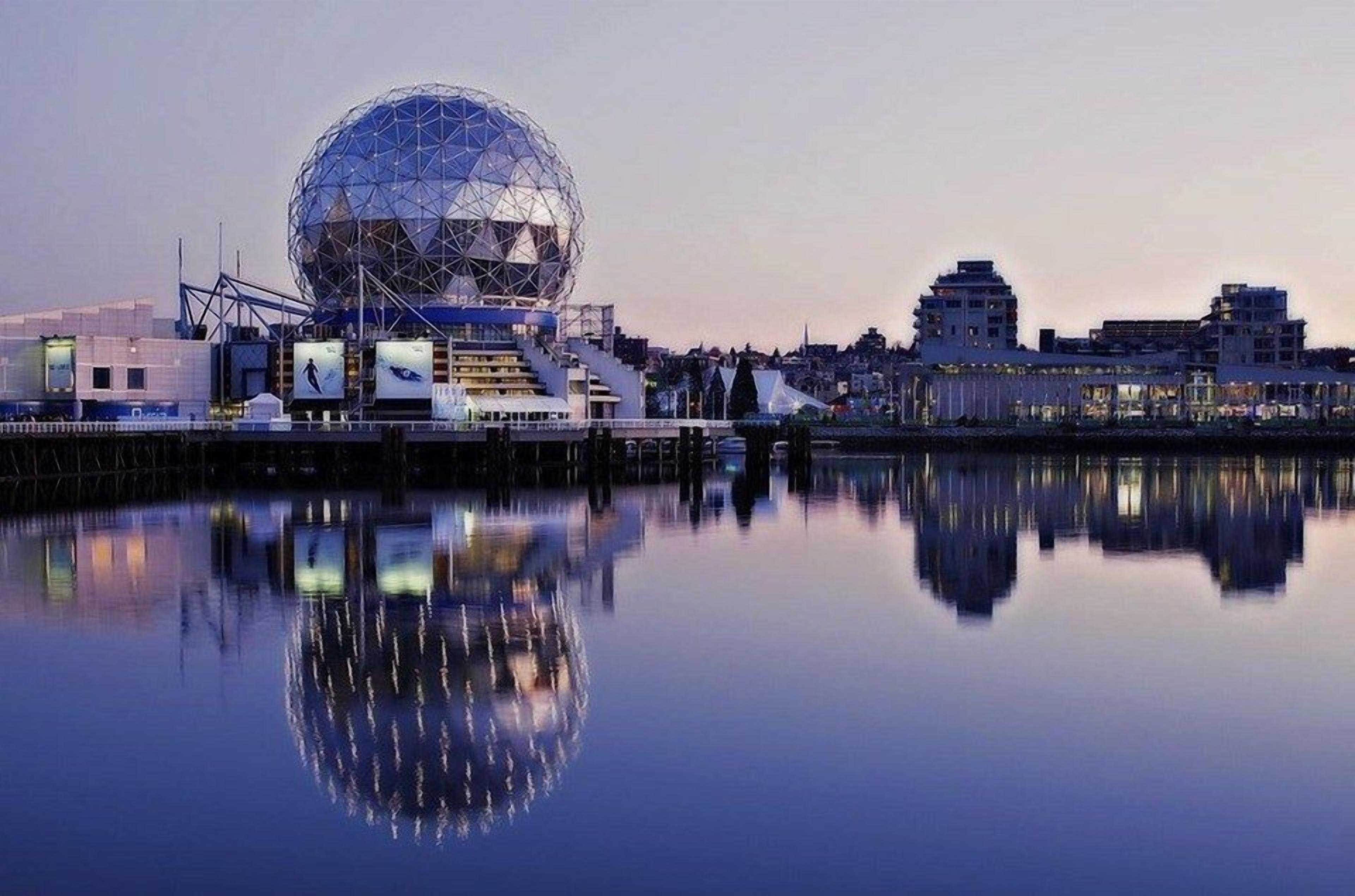 A modern building with a large spherical structure, a waterfront, and a reflection in the water.