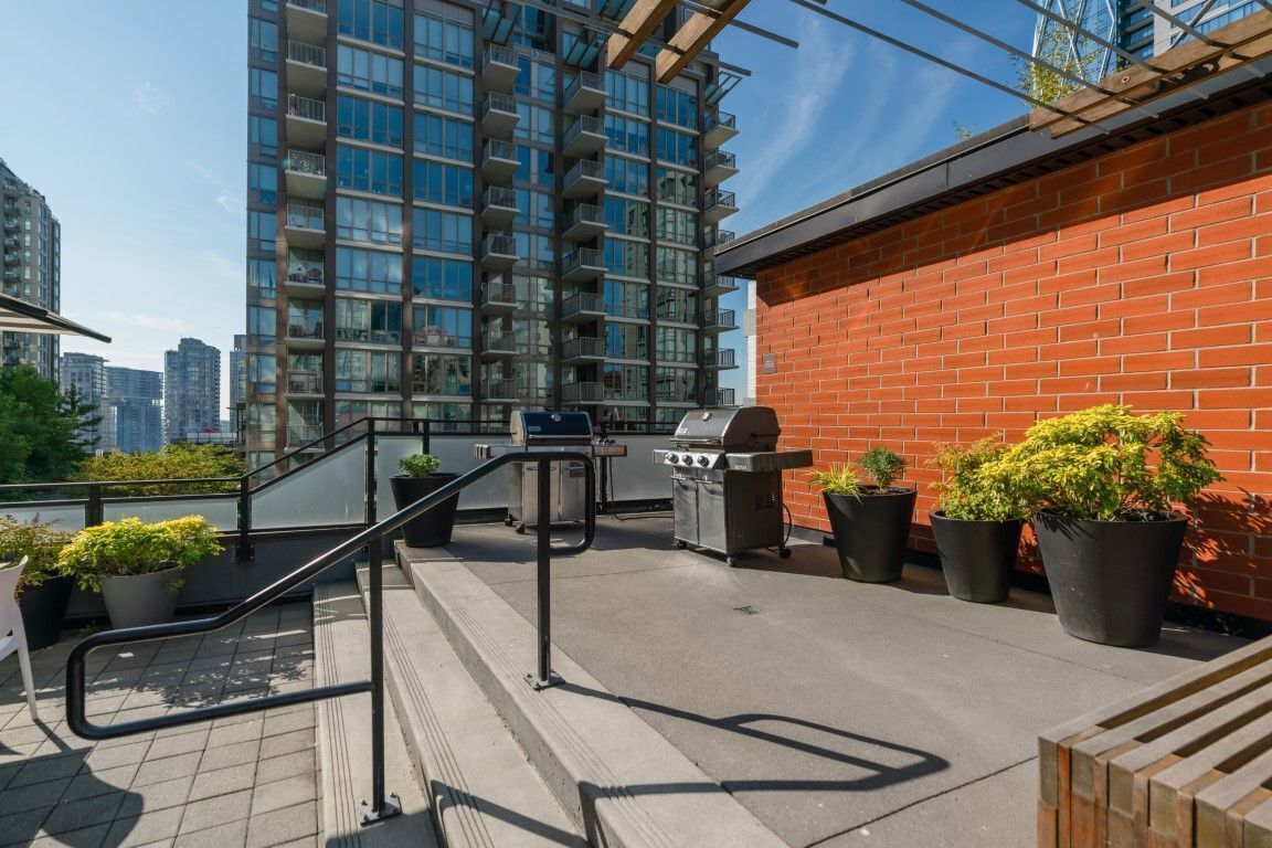 Eine Dachterrasse mit Grill, Topfpflanzen und Blick auf ein Hochhaus.