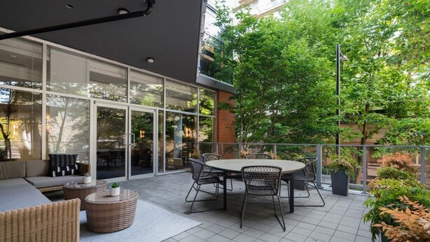 A modern outdoor patio with a round table and chairs, a sofa, and potted plants.