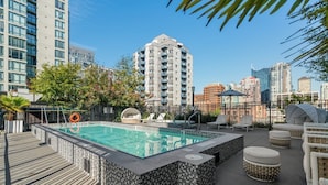 A rooftop pool area with a tiled deck, lounge chairs, and a view of the city skyline.