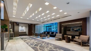 A modern lobby with a long, patterned carpet, a sofa area, and a TV screen.